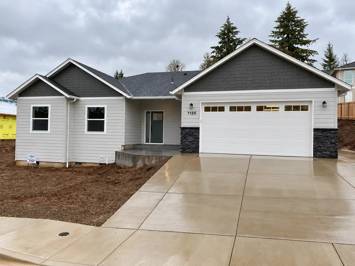Custom home built by MP Construction, light gray lap siding with charcoal shake gables, a stone-trimmed two-car garage and a new concrete drive